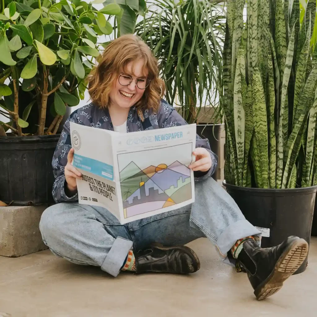 Subscriber reading a colorful good news newspaper surrounded by green plants